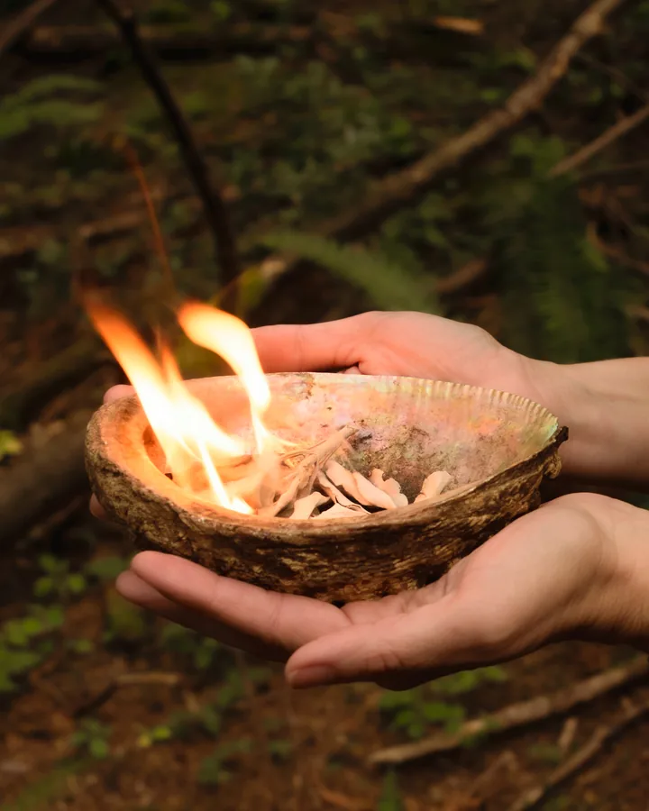 A small flame burning in an abalone shell held in two hands