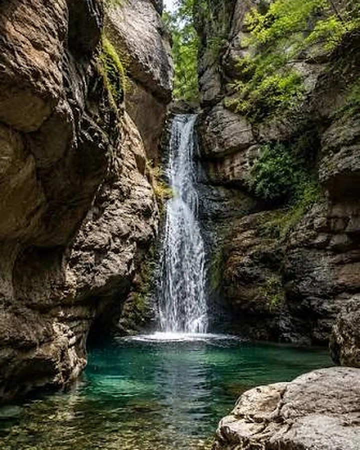 A waterfall pouring into a clear green pool between mossy rock walls